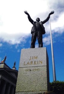 Colour photograph showing the sculpture of Jim Larkin, with the Spire, in front of the General Post Office on O'Connel Street, Dublin.